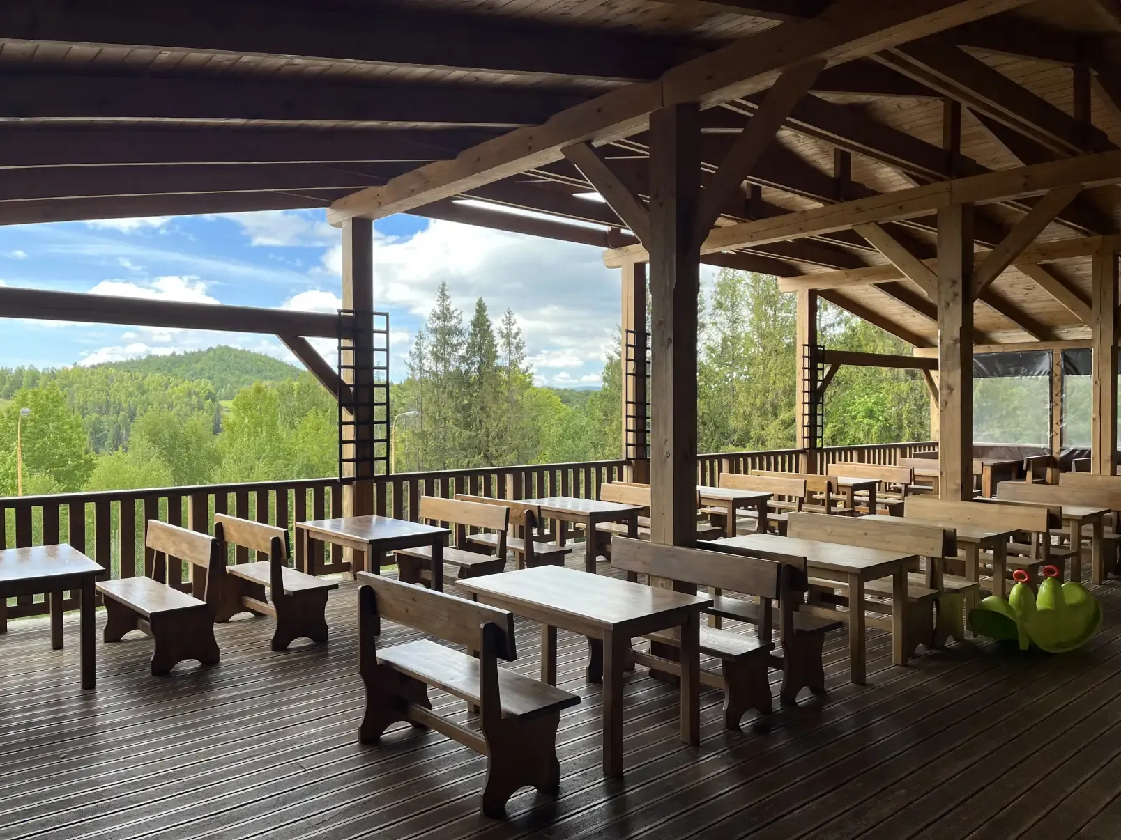 A covered wooden terrace with tables and a view of the wooded ridges of Muránska planina
