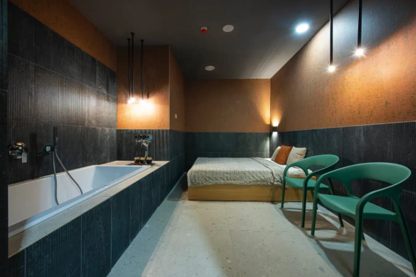 The beer bath room, with a tub set into dark tiling, a bed and two green chairs
