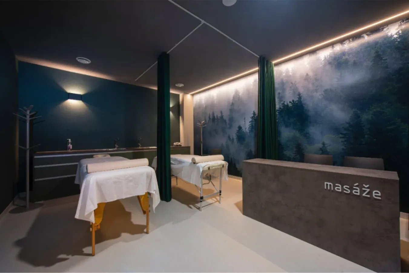 Two massage beds separated by a curtain, with a photo mural of a misty forest on the wall