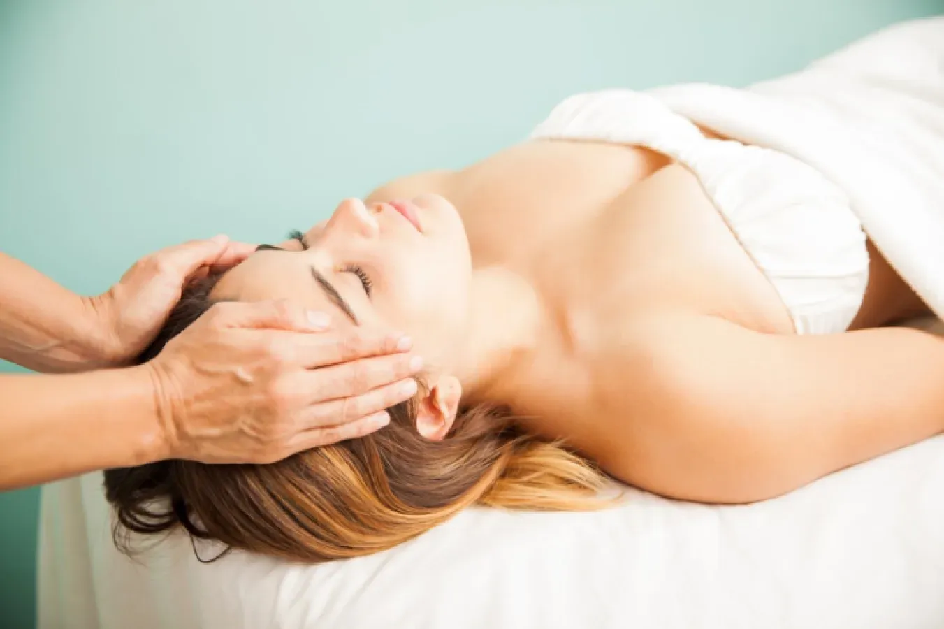 A therapist resting her palms on the forehead and temples of a woman lying with her eyes closed