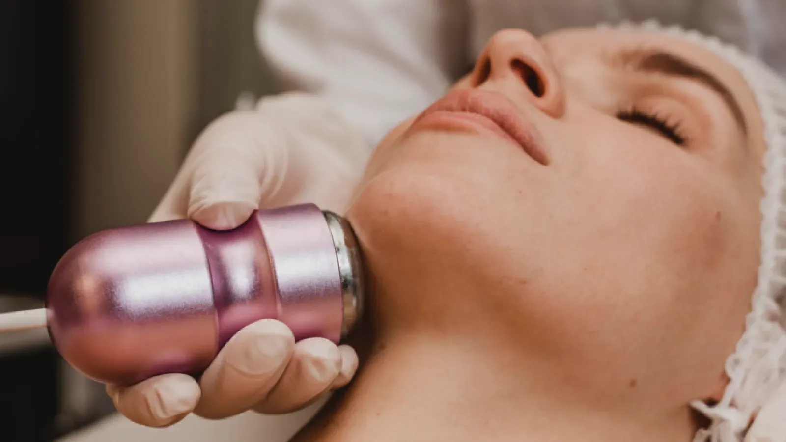 A gloved beautician treating the skin of a client's neck with an oxygen device