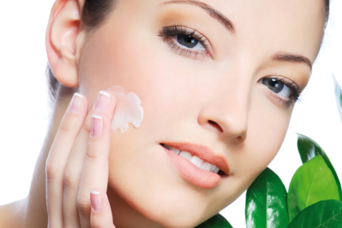 A woman applying cream to her cheek, with green leaves in the corner
