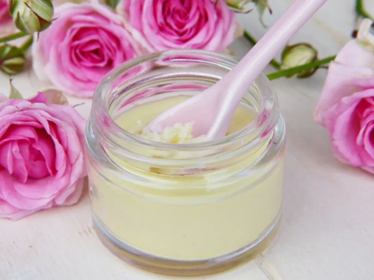 An open jar of face cream with a spatula, among pink roses