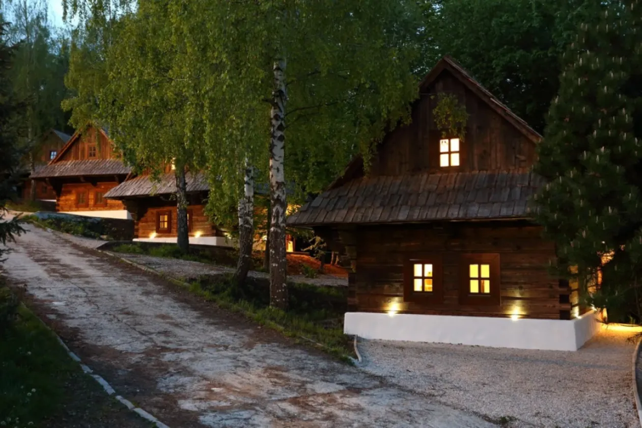 A lit wooden cottage among birch trees after dark