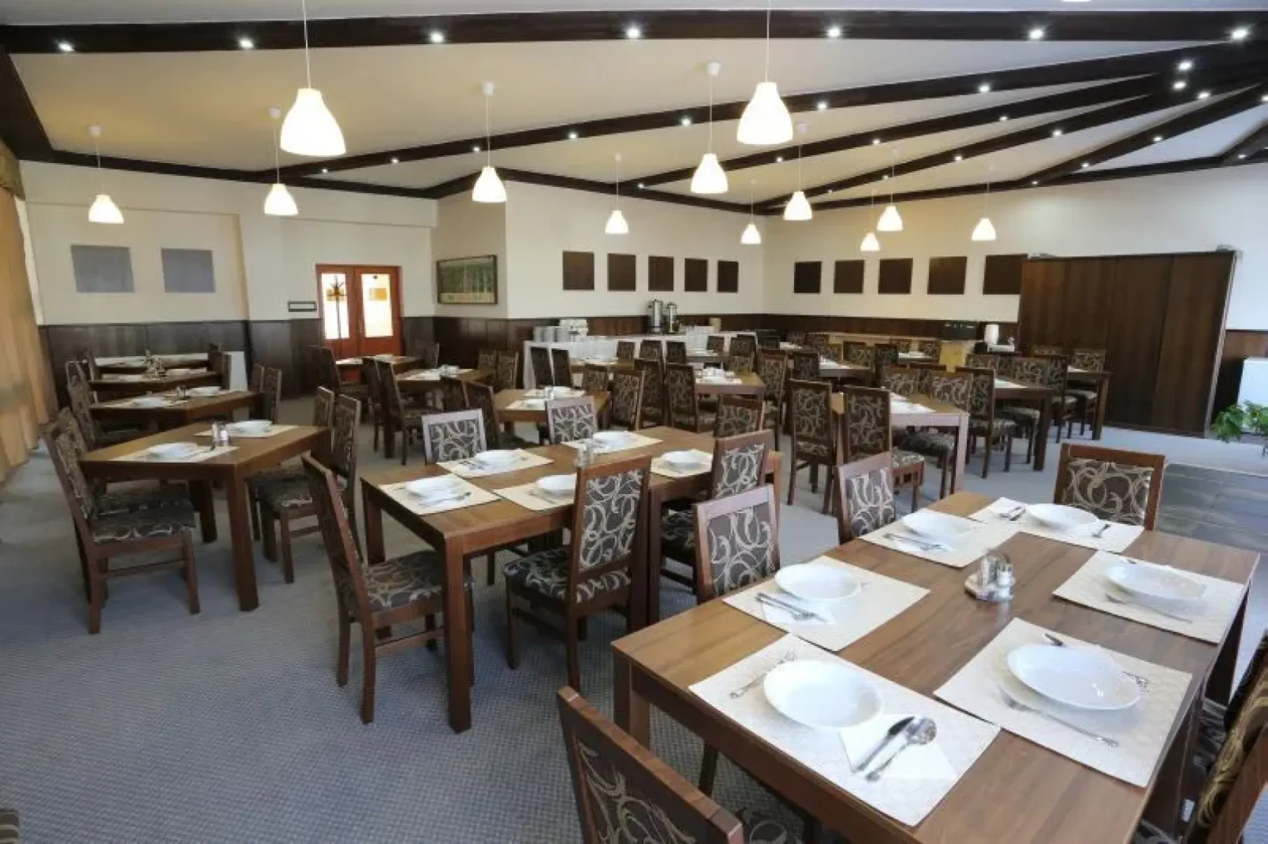 A dining room with laid tables beneath a timber-beamed ceiling